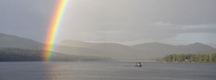 Vivid rainbow shining over calm lake with pontoon boat in countryside