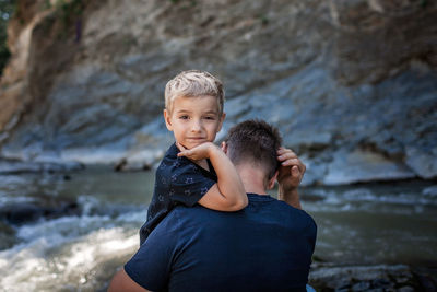 Like father like son. middle aged father embracing cute little son on the bank of river