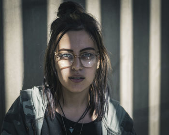 Portrait of young woman wearing eyeglasses against wall