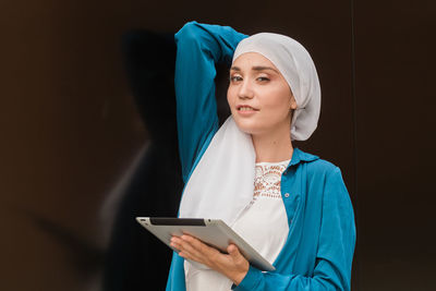 Portrait of young woman using mobile phone while standing against wall