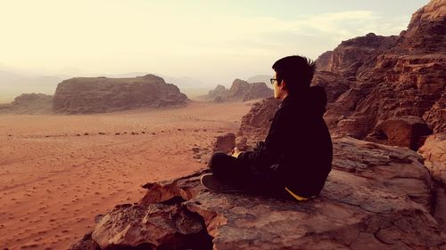 Rear view of woman sitting on rock formation against sky