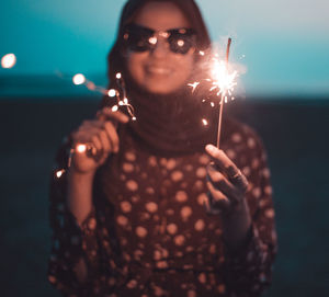 Young woman with illuminated sparklers standing at beach during dusk