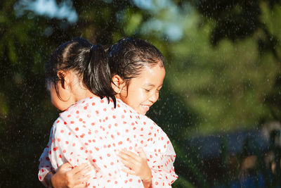 Girls wearing raincoats embracing in rain