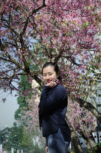 Portrait of young woman standing by tree in bloom