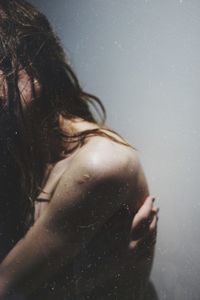 Side view of shirtless young woman standing against wall