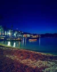 Illuminated city by sea against clear sky at night