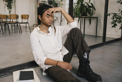 Full length of young non-binary professional sitting depressed at office