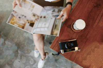 Low section of woman reading magazine while sitting by table with camera and coffee