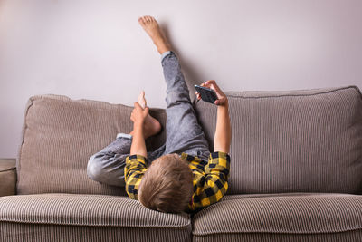 Boy using phone while lying down on sofa