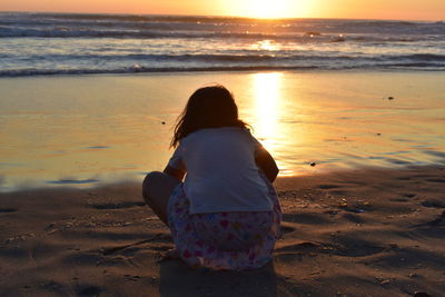 Rear view of woman standing at beach during sunset