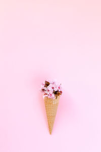 Close-up of ice cream cone with flowers against pink background