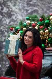 Portrait of smiling young woman holding christmas tree during winter