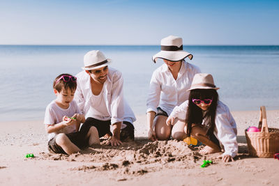 People sitting on beach by sea against sky