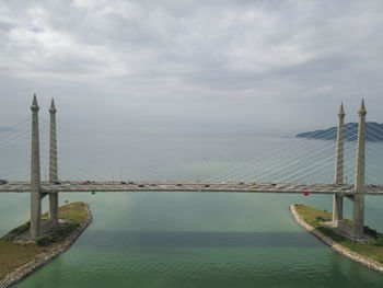 Suspension bridge over river against cloudy sky