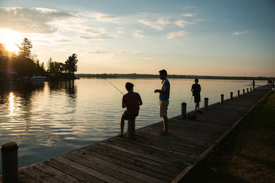 Father and sons fishing on dock of lake at sunset in ontario, canada.