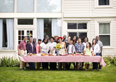 Portrait of happy family and friends standing at table against house