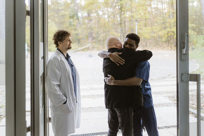 Senior male patient embracing nurse while standing by doctor at hospital doorway