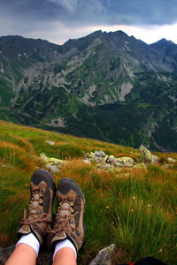 Low section of man standing on mountain against sky