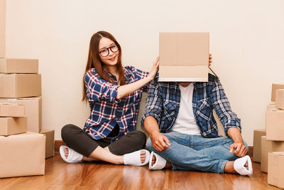 Woman putting box on boyfriend while sitting on floor at new home
