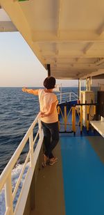 Rear view of man standing on railing against sea