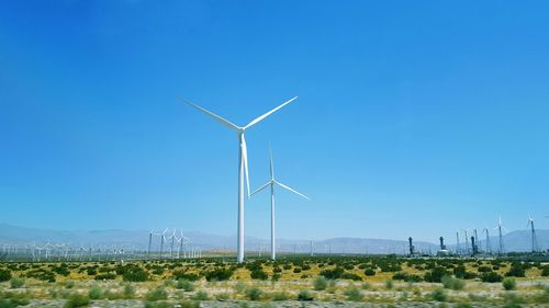 Wind turbines on field against clear blue sky