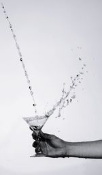 Cropped hand holding drink glass against white background