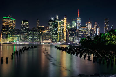 Illuminated buildings by river against sky at night