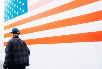 Rear view of man walking by american flag painted on wall