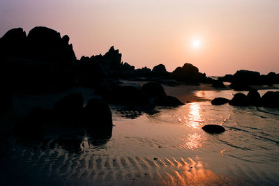 Silhouette rocks on beach against sky during sunset