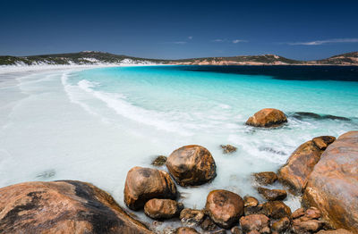 Scenic view of rocks on beach against blue sky