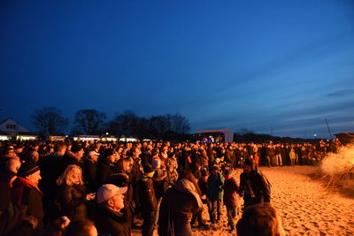 Crowd standing in illuminated beach against blue sky at dusk