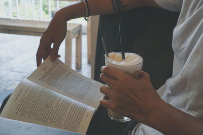 Midsection of man reading book while holding drink