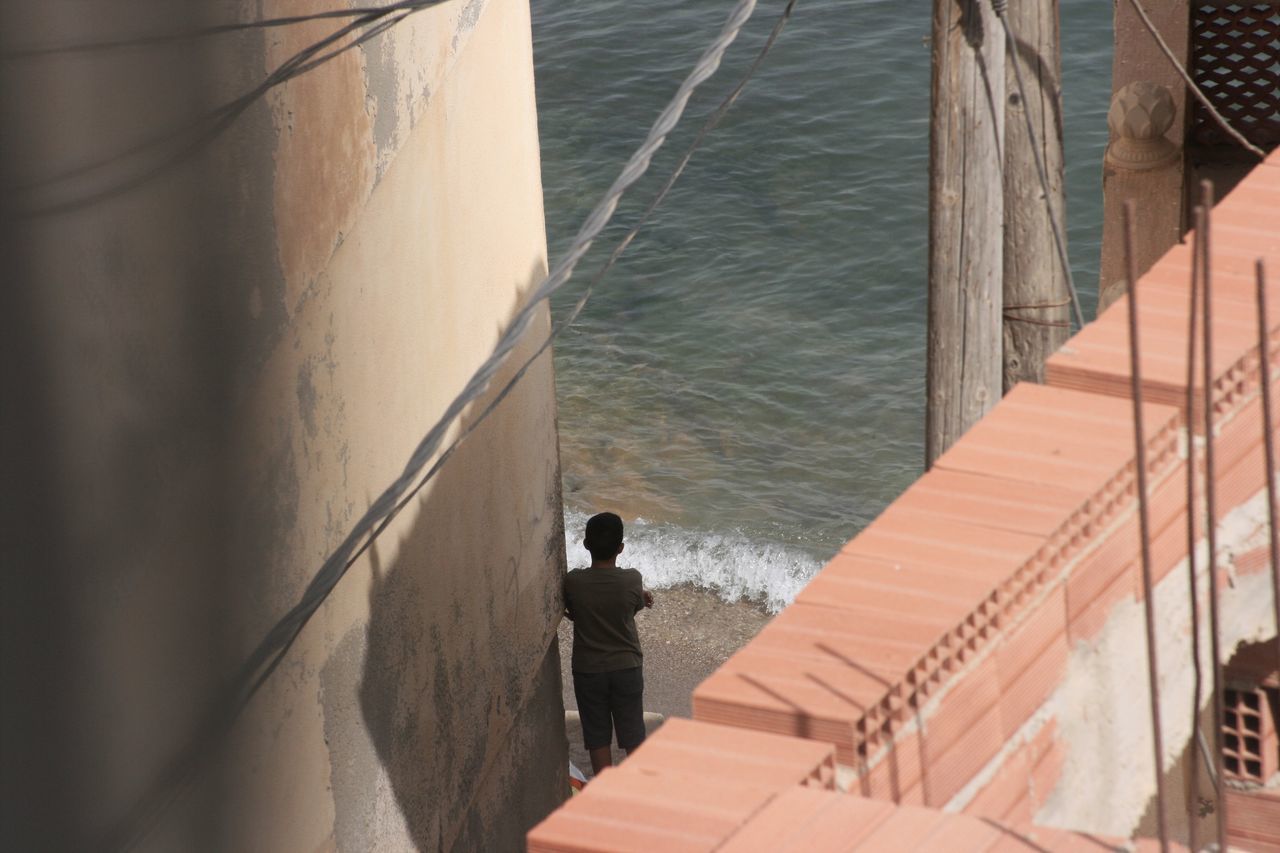 HIGH ANGLE VIEW OF MAN STANDING AT SEA