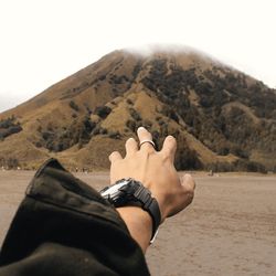 Cropped hand of person reaching towards mountain on land