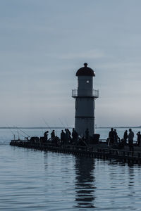 People on lighthouse by sea against sky