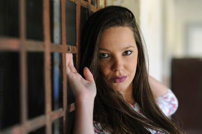 Portrait of young woman standing by rusty metal grate