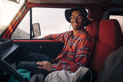 Smiling young man wearing plaid shirt while sitting in van on vacation