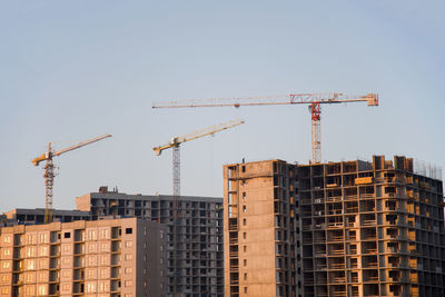 Low angle view of cranes on buildings against clear blue sky