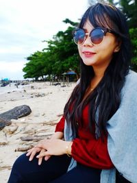 Portrait of young woman wearing sunglasses while sitting at beach