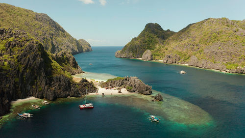 Tropical landscape bay with beach and clear blue water surrounded by cliffs, aerial drone. 