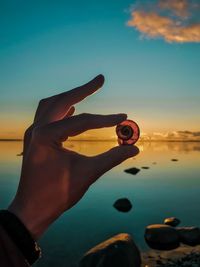 Midsection of person holding sea against sky during sunset