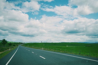 Empty road amidst field against sky