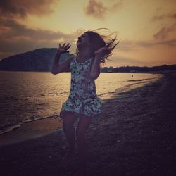 Girl standing at beach against sky during sunset