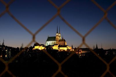 Illuminated buildings against clear sky seen through chainlink fence