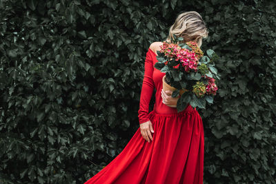 Midsection of woman with hydrangea dressed in red standing against dark wall