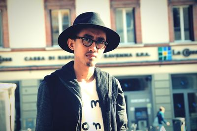 Portrait of young man in hat and eyeglasses against building