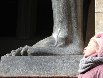 Side view of cute girl puckering by statue in city