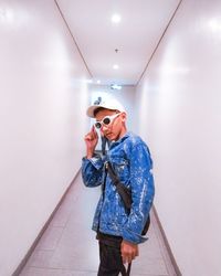 Young man wearing sunglasses standing amidst white wall