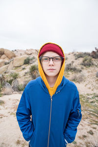 Tween with beanie and glasses in front of small mound in desert