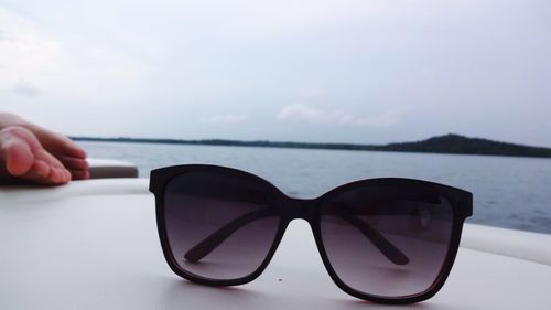 Close-up of hand wearing sunglasses against sky